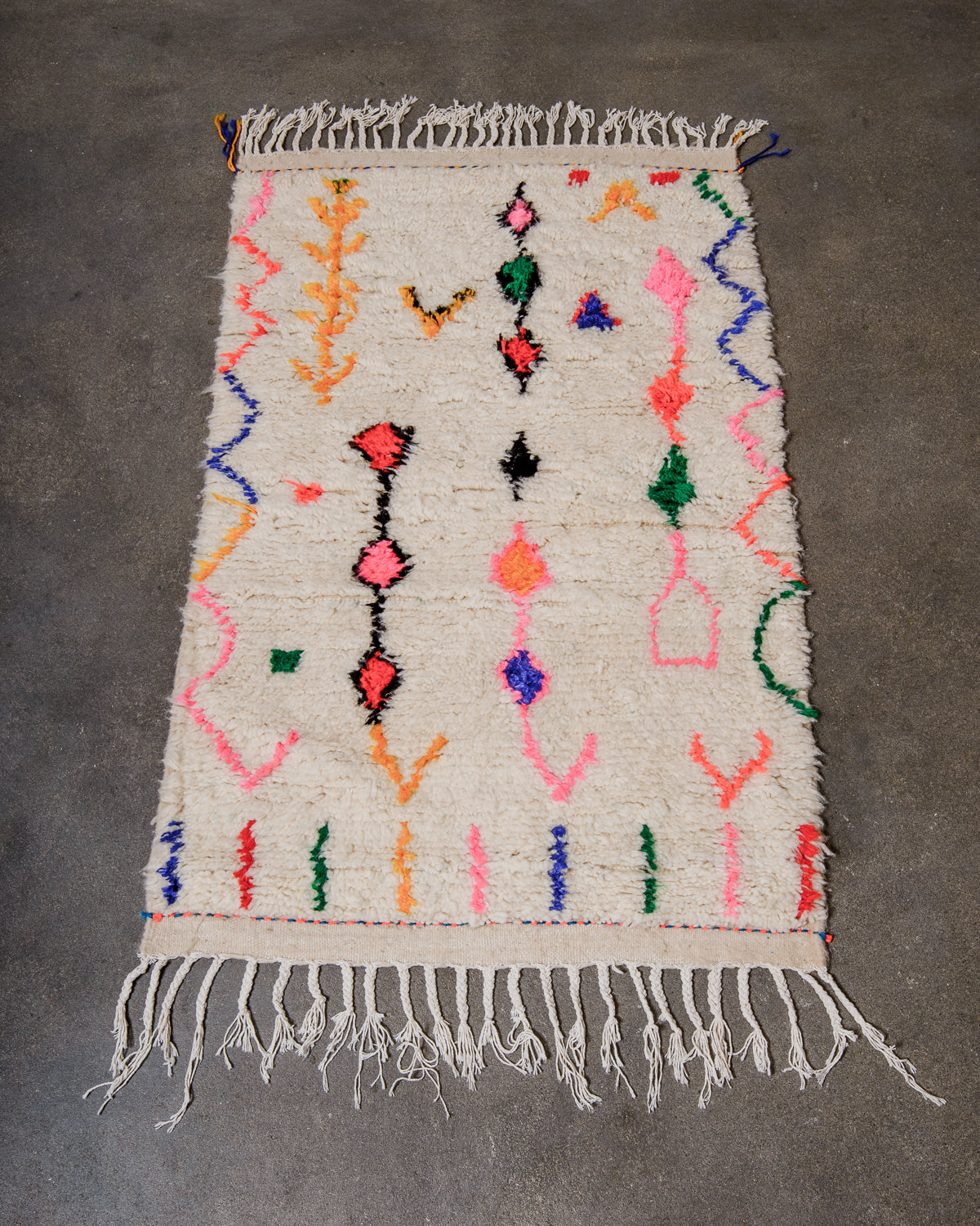 Cream wool Azilal rug with colourful cotton design laying on a concrete floor.
